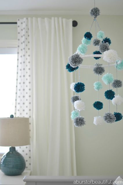 A DIY pom-pom mobile made from yarn and an embroidery hoop is a fun and stimulating addition to your little one's nursery. Find the full tutorial at www.aburstofbeautiful.com | A Burst of Beautiful 